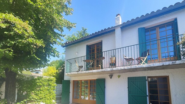 Un edificio de dos pisos con balcón, contraventanas verdes y fachada blanca.