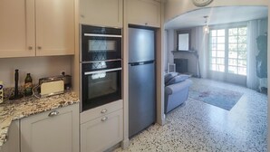 Cocina compacta con horno integrado, refrigerador y comedor con mesa y sillas.