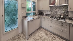 Una cocina con encimeras de granito, armarios blancos, estufa a gas y una ventana con vidrio tipo diamante.