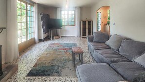 Una sala de estar con un sofá gris, un tapete estampado, un televisor y un armario.