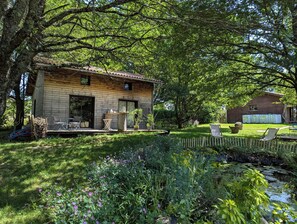 Eine Holzhütte mit einer Veranda, umgeben von üppigem Grün und einem kleinen Teich.