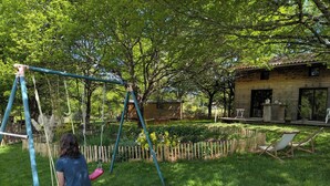 A person on a swing in a grassy area with trees and a wooden house in the background. - La Chambre d'Art in the heart of nature, 300 metres from Lake St Pardoux (Saint-Pardoux-le-Lac)