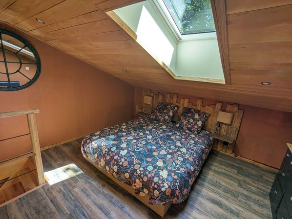 Un dormitorio con tragaluz, cabecera de madera y colcha estampada.