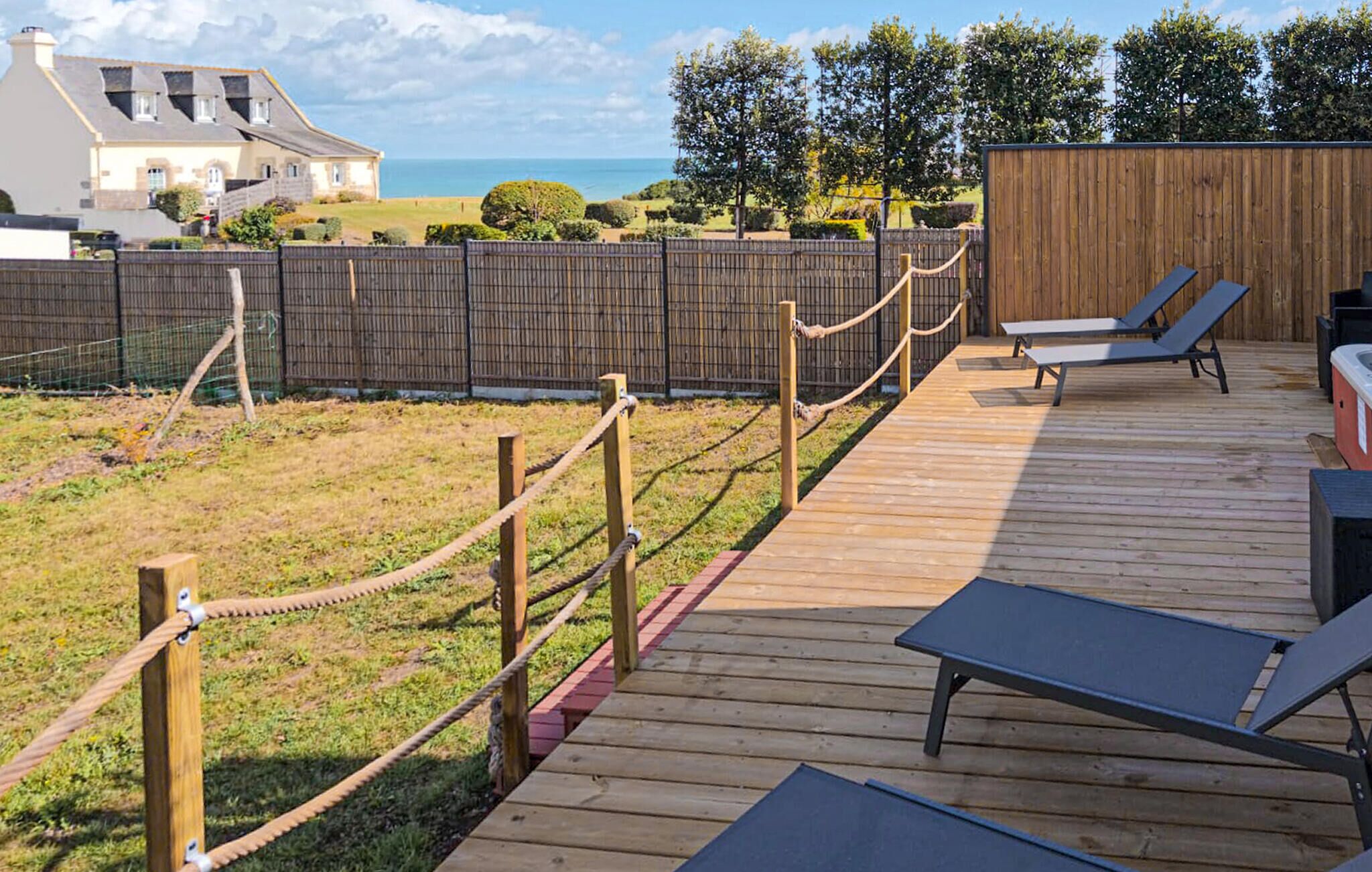 A wooden deck with lounge chairs and a hot tub, overlooking a grassy area and a wooden fence.