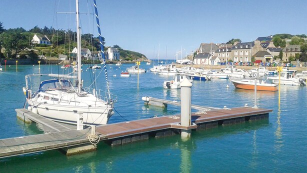 Un puerto deportivo con varias embarcaciones amarradas, un muelle y edificios al fondo.