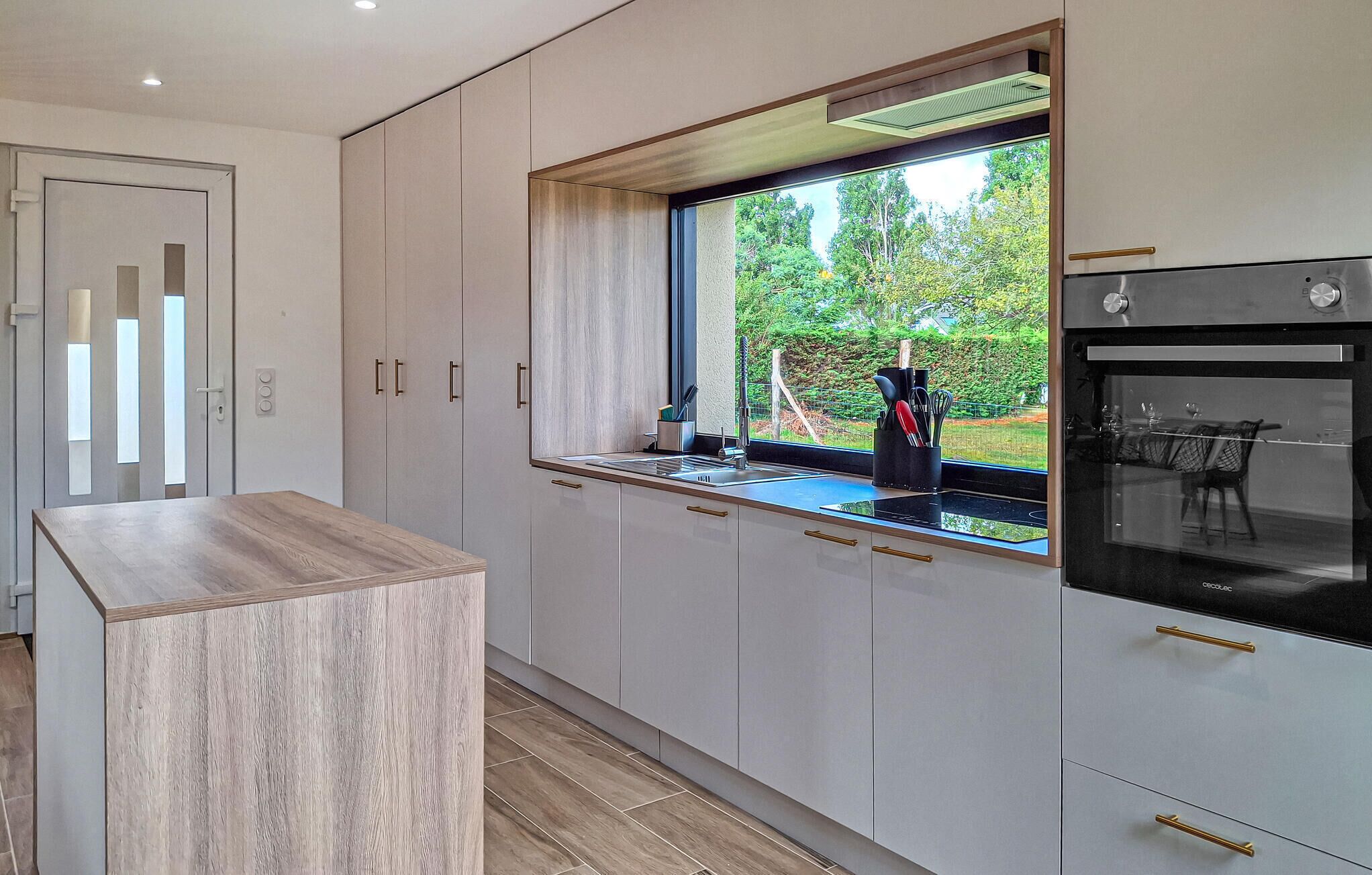 A modern kitchen with a large window, built-in oven, and minimalist cabinetry.