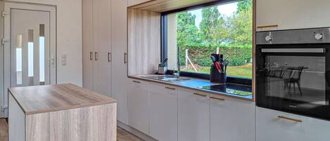 A modern kitchen with a large window, built-in oven, and minimalist cabinetry.