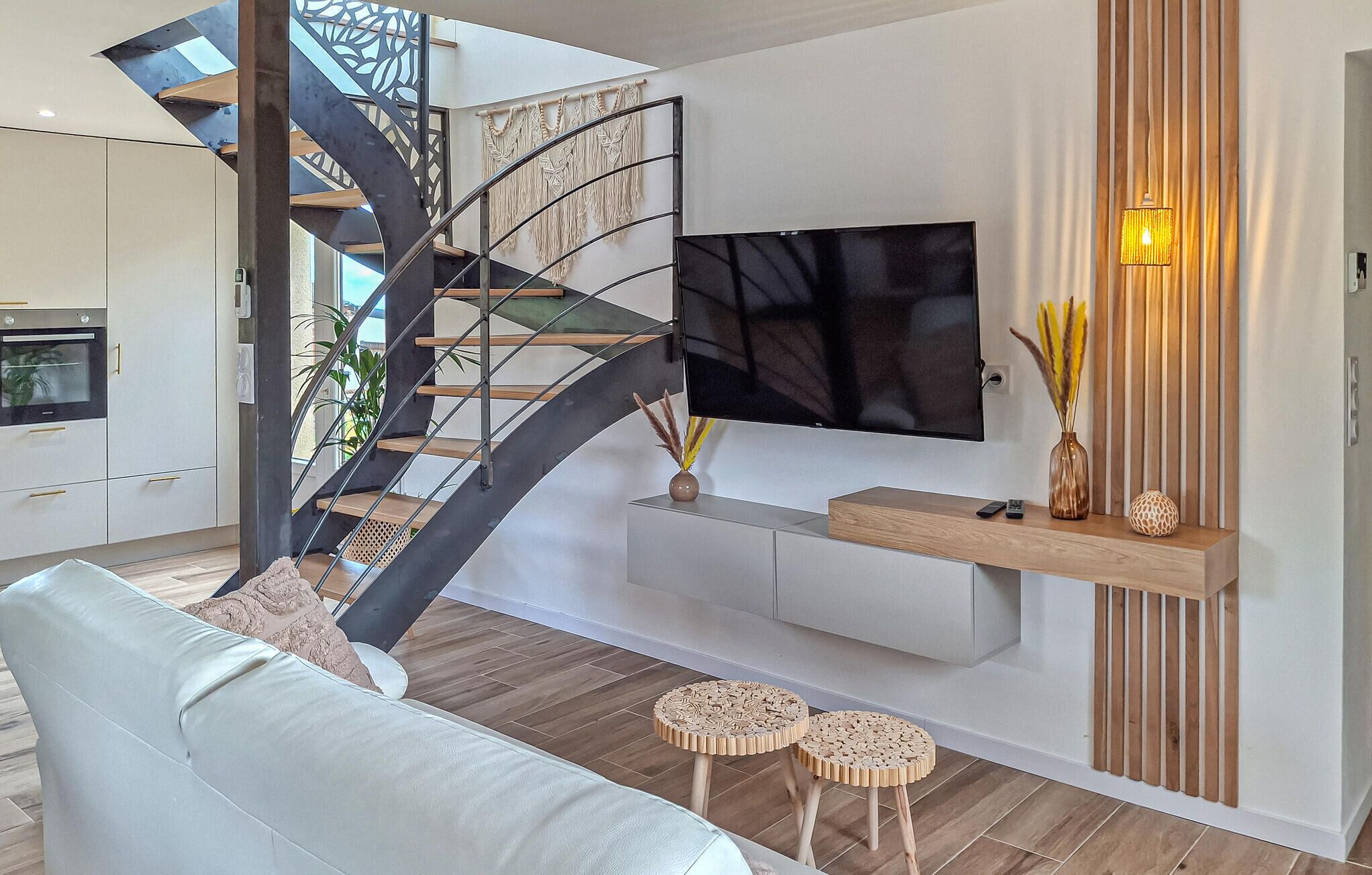 Un salon moderne avec un escalier à volutes, un téléviseur fixé au mur et une console en bois.