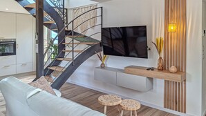 Una sala de estar moderna con una escalera curva, un televisor montado y una mesa consola de madera.