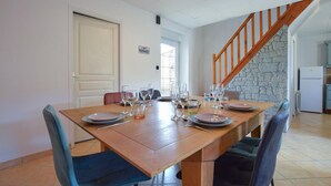 Een eetruimte met een houten tafel voor zes personen, omringd door stoelen, in een kamer met een stenen muur en een houten trap.