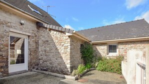 Een stenen gebouw met een deur en raam, een klein tuin met planten en bloemen, en een helderblauwe lucht.