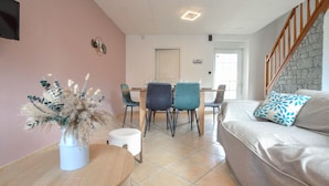 Een moderne woonkamer met een bank, een eettafel met stoelen, een decoratieve vaas en een trap.