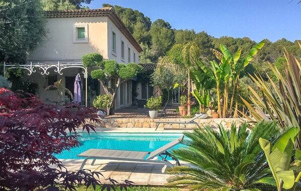 A pool area with lounge chairs, a stone wall, and tropical plants. - Stunning home in Speracedes (Speracedes)