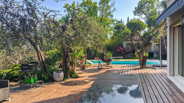 A wooden deck with a pool, surrounded by lush greenery and trees.