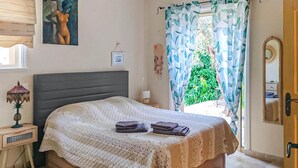 A bedroom with a bed, a nightstand, a lamp, a framed picture, and a window with curtains.