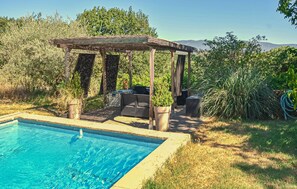 A swimming pool with a pergola and outdoor furniture, surrounded by greenery and hills in the background.