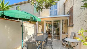 Ein möblierter Terrassenbereich mit Tisch, Stühlen und einem grünen Sonnenschirm, sowie eine Glastür zu einem überdachten Bereich.