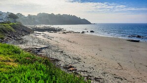 A coastal beach with a rocky shoreline, grassy areas, and a view of the ocean.