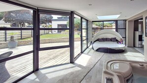 A modern bedroom with a curved bed, large windows, and a view of the outdoors.