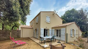Una casa de dos pisos con un patio, una mesa y sillas, y una silla rosa.