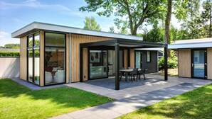 Ett modernt hus med stora glasfönster, en täckt uteplats och en välskött gräsmatta.