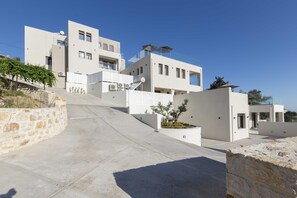 A modern multi-story building with a flat roof, large windows, and a stone retaining wall.