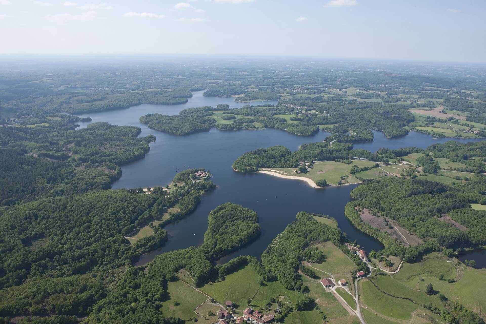 An aerial view of a lakeside area with multiple islands, surrounded by dense forests and open fields.