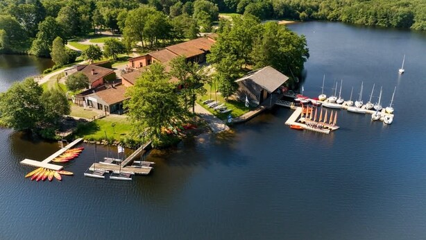 Una propiedad junto al lago con un muelle, barcos y un edificio rodeado de árboles.