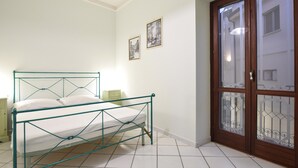 Een slaapkamer met een metalen bed, witte wanden en een houten deur met glaspanelen.
