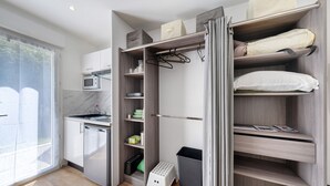 Cocina compacta con microondas, refrigerador pequeño y un taburete.