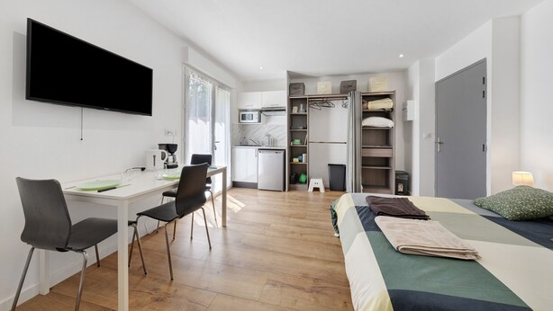 Una habitación pequeña con cama, escritorio y kitchenette.