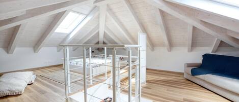 A high-ceilinged attic room with a metal staircase, wooden flooring, a white sofa, and a skylight.