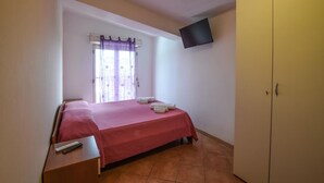 Een slaapkamer met een bed, nachtkastje, televisie aan de muur en een kledingkast.