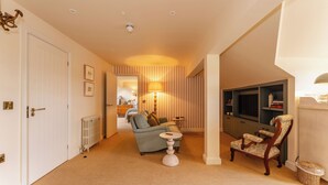 A cozy living room with a sofa, armchair, and a small table. There is a radiator, a lamp, and a television on the wall. - Three Acres Inn & Restaurant (Huddersfield)