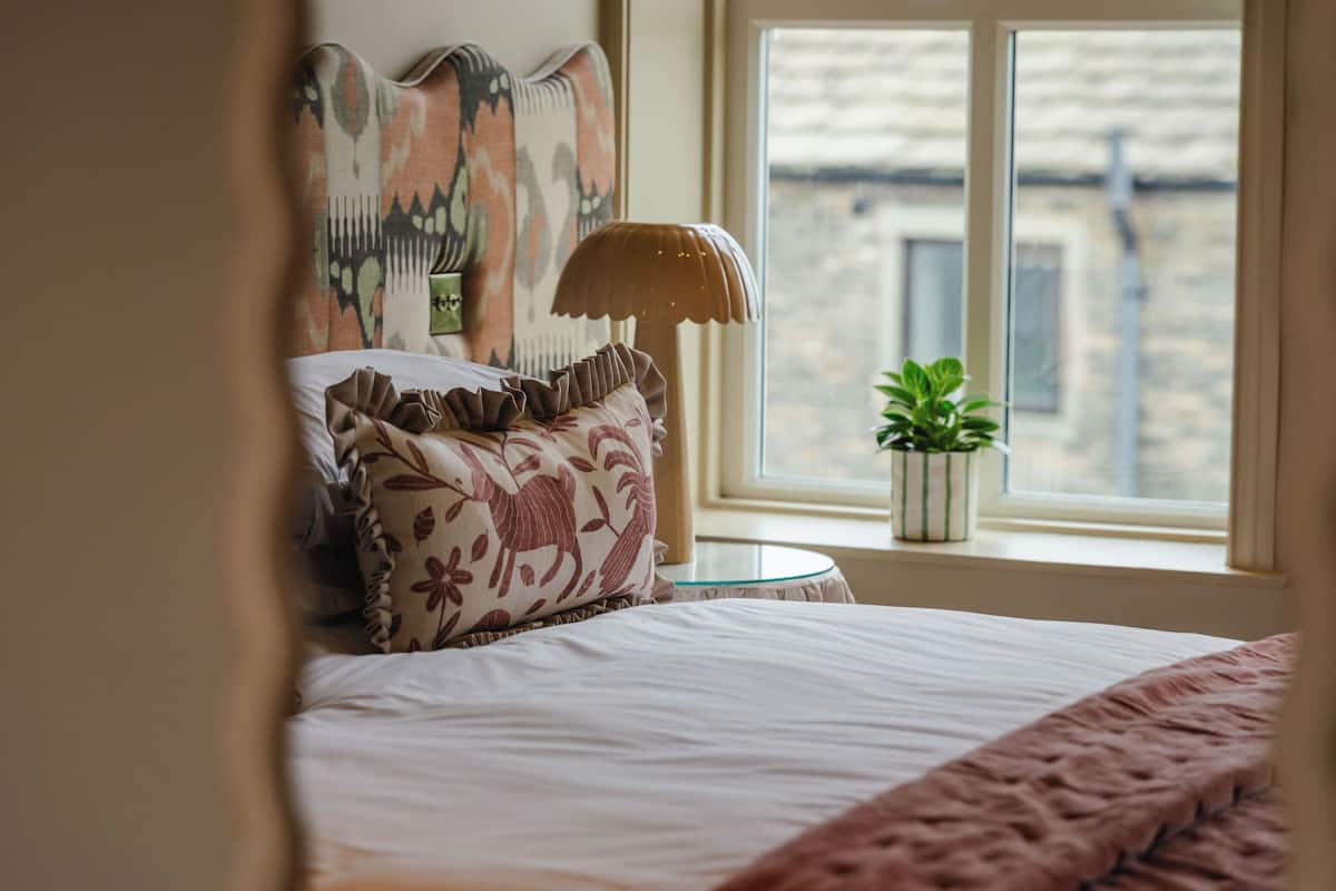 A neatly made bed with patterned pillows, a bedside lamp, and a view of the city through a window.