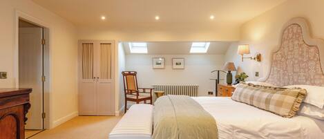 A bedroom with a large bed, a wooden bench, a desk, and a radiator.