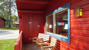 En rødmalede træbygning med en veranda, hvor der er træbænke og et vindue med en lampe.
