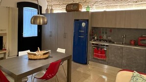 Une cuisine moderne avec un réfrigérateur bleu, une cuisinière à gaz et un four à micro-ondes. On y trouve une table à manger avec des chaises rouges et un panier posé dessus.
