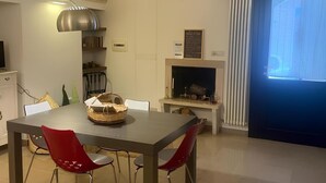 Un espace repas comprenant une table et des chaises, un luminaire suspendu, une cheminée et une grande fenêtre avec des stores.