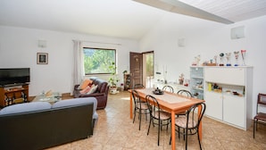 Un salón espacioso con un sofá, una mesa de comedor con sillas, un televisor y un mueble con diversos objetos.