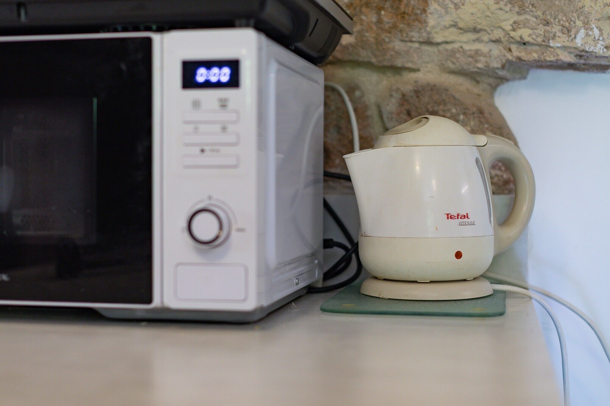 Un forno a microonde con display digitale, una macchina da caffè bianca e un sottobicchiere verde su un piano di lavoro.