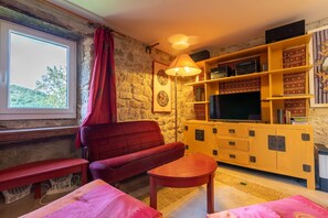 A cozy living room with a red sofa, a wooden coffee table, a TV on a wooden cabinet, and a lamp. - Holiday Home 'La Treille' with Mountain View and Wi-Fi (Saint-Barthélemy-Grozon)