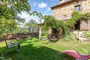 A stone house with a stone wall, a patio with a table and chairs, and a grassy yard. - Holiday Home 'La Treille' with Mountain View and Wi-Fi (Saint-Barthélemy-Grozon)