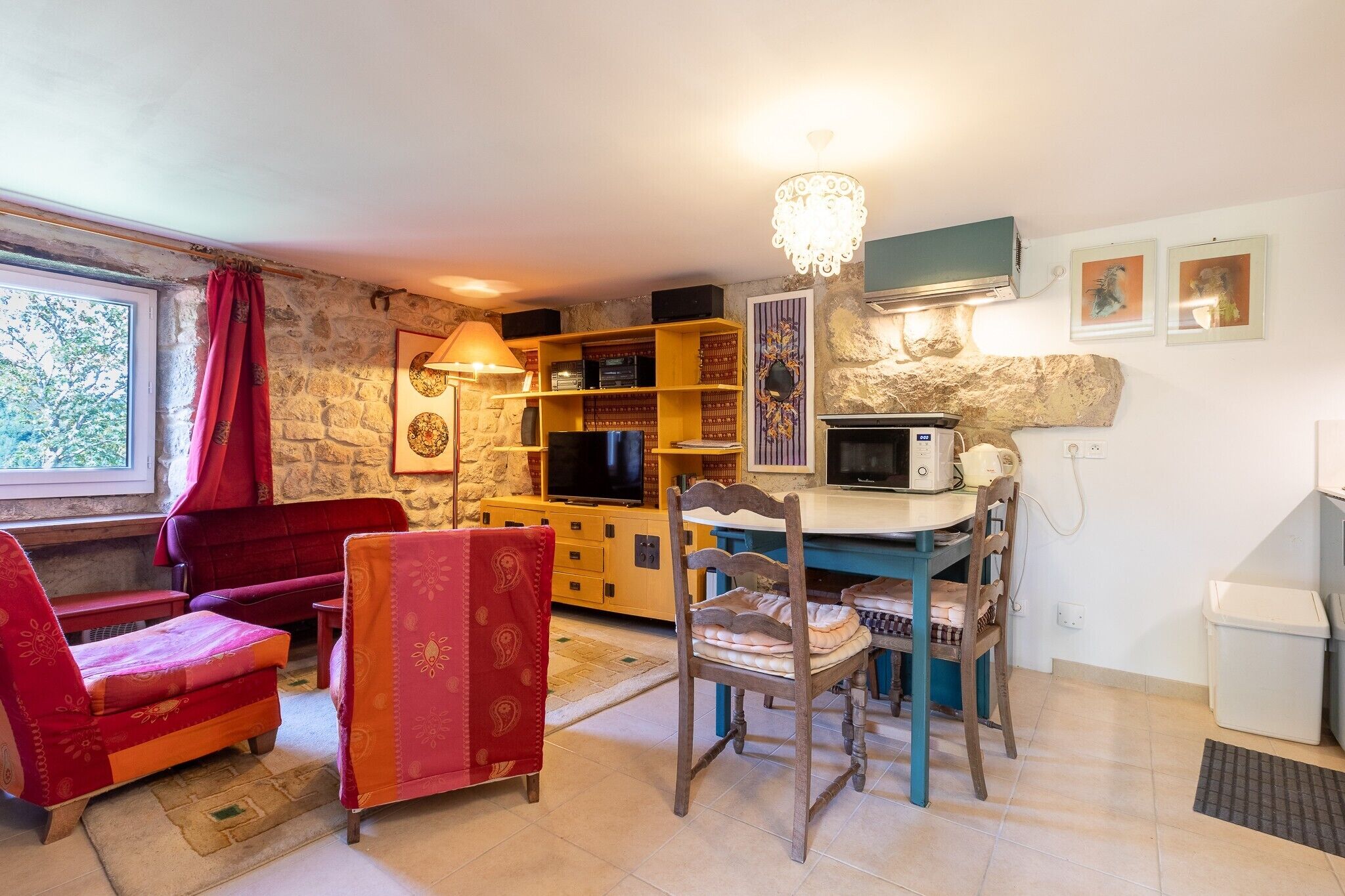 A cozy living room with a stone wall, a television, a bookshelf, a dining table, and a red sofa.