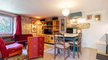 A cozy living room with a stone wall, a television, a bookshelf, a dining table, and a red sofa.