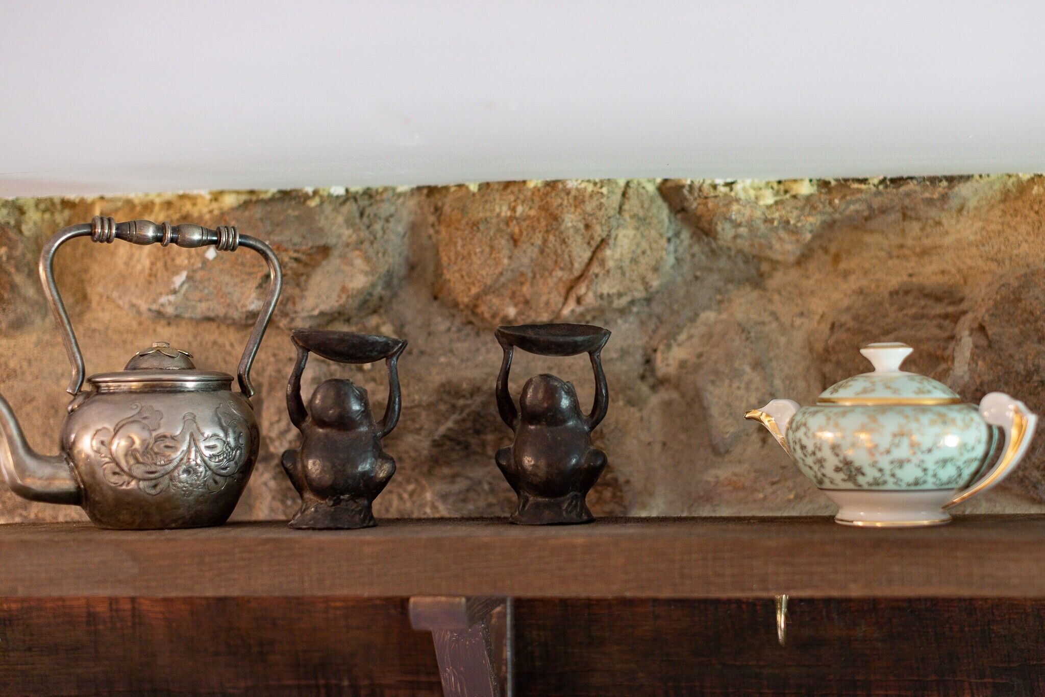 A shelf with three tea sets against a stone wall.