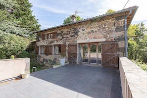 A stone building with a patio, wooden shutters, and a metal roof.