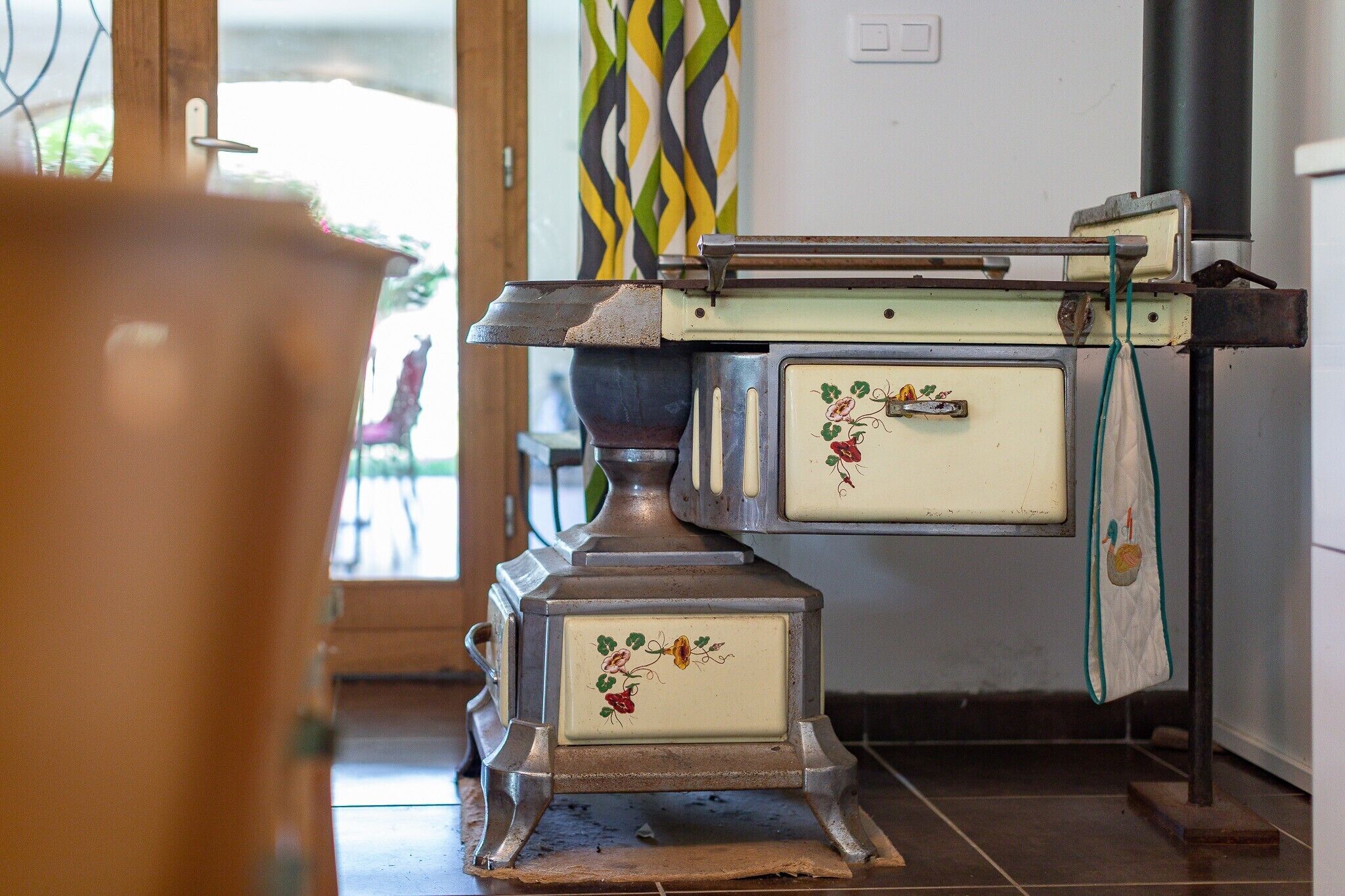 A vintage stove with a floral design, a metal rack, and a white cabinet with a handle.