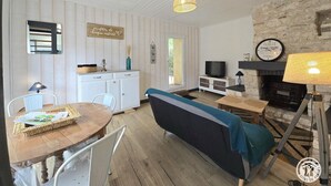 A cozy living room with a stone fireplace, a television, and a dining area with a wooden table and chairs.