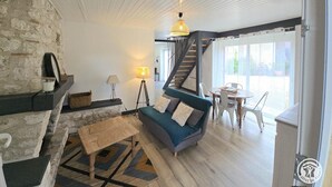 A cozy living room with a stone wall, a blue sofa, a wooden coffee table, and a staircase leading to a balcony.